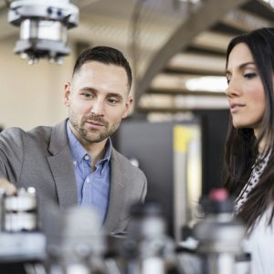 Businessman and businesswoman examining workpieces in factory Businessman and businesswoman examining workpieces in factory